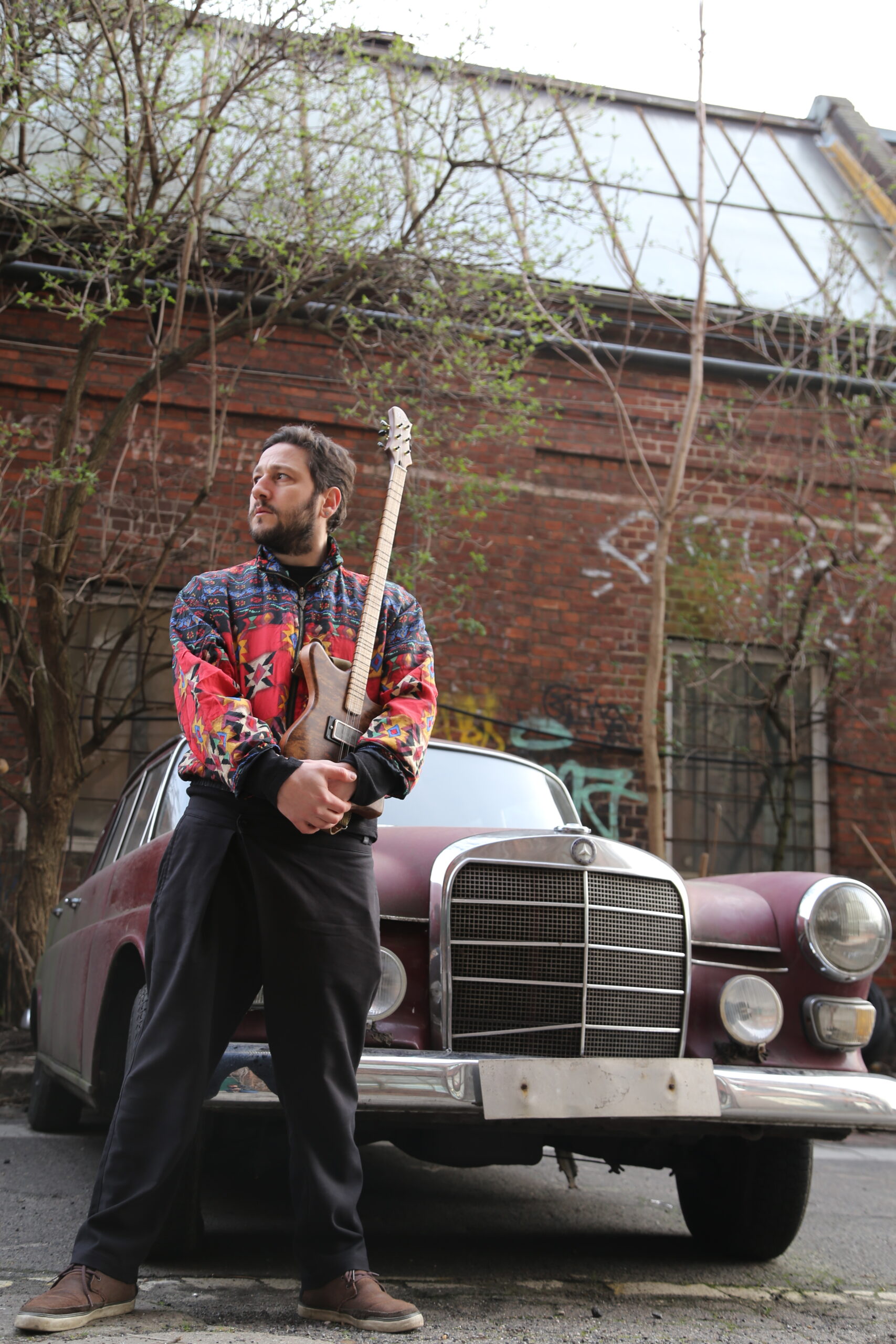 Mahir posing with a guitar next to a vintage car